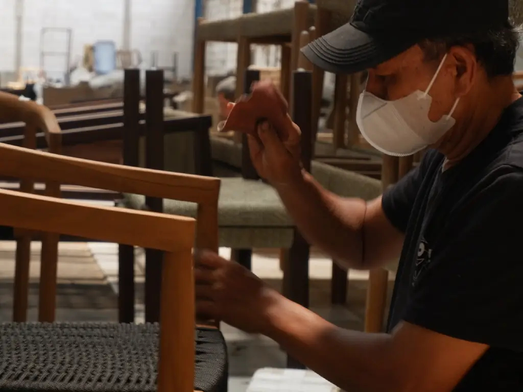 Craftsman sanding teak panel sample for SVLK certification with quality-control tag at Indonesian furniture manufacturer