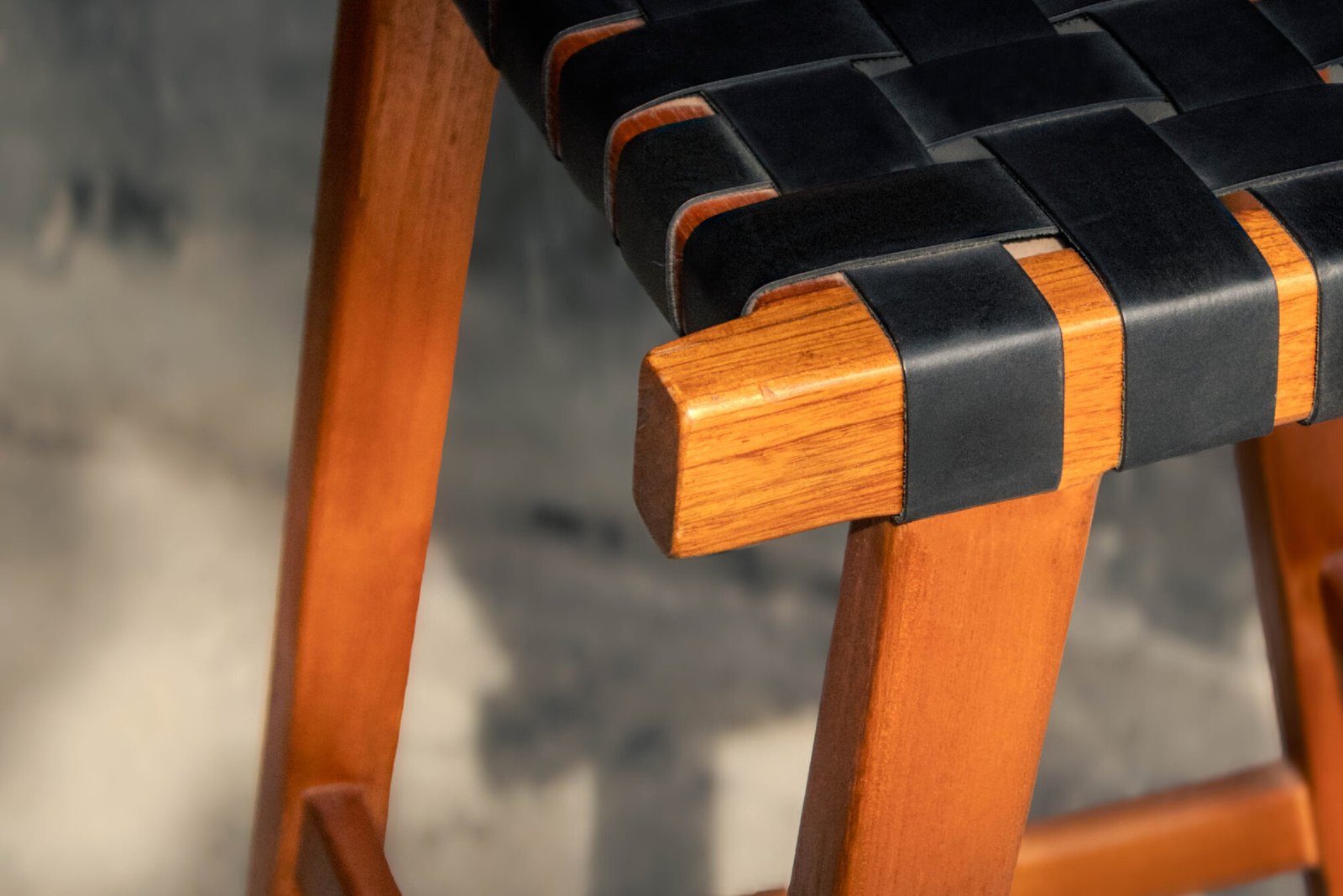 Close-up of a leather woven bar stool featuring black leather straps handwoven over a teak wood frame, crafted by Indonesian furniture manufacturers for modern and minimalist interiors.