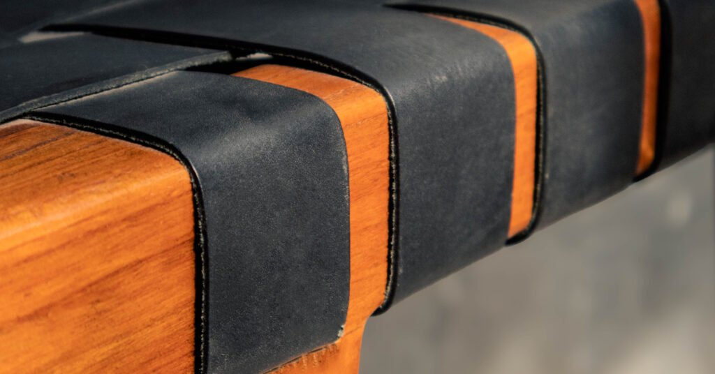 Macro shot of leather weaving on backless bar stool, featuring the natural texture of black leather and the warmth of teak from trusted Indonesian furniture suppliers.