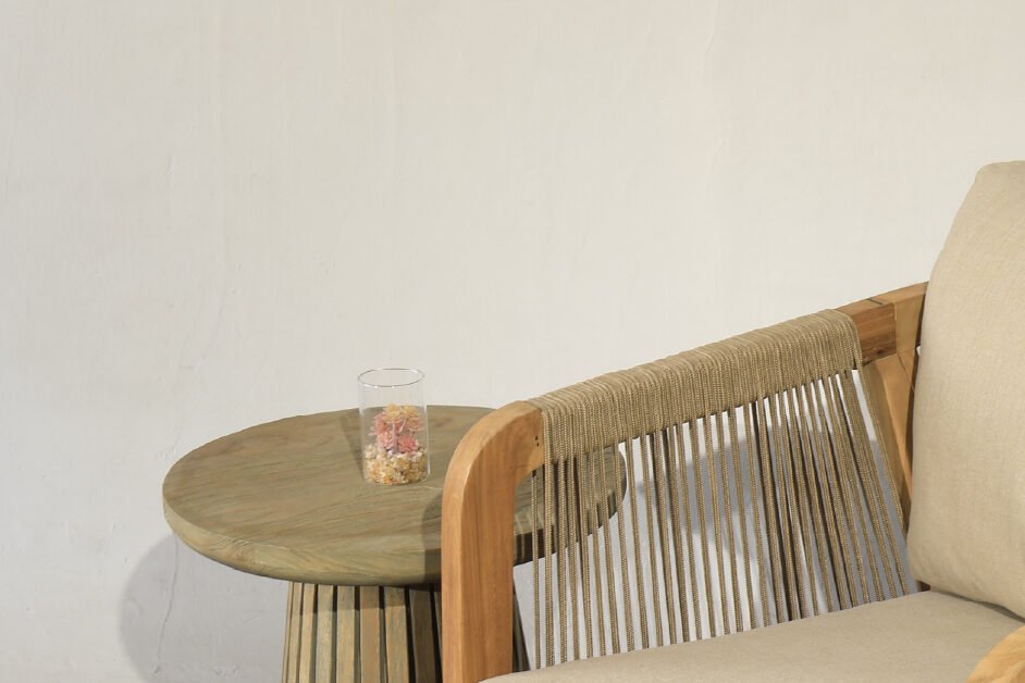 Teak lounge chair with rope accents and beige cushion next to a round teak side table, ideal for modern indoor and outdoor settings.