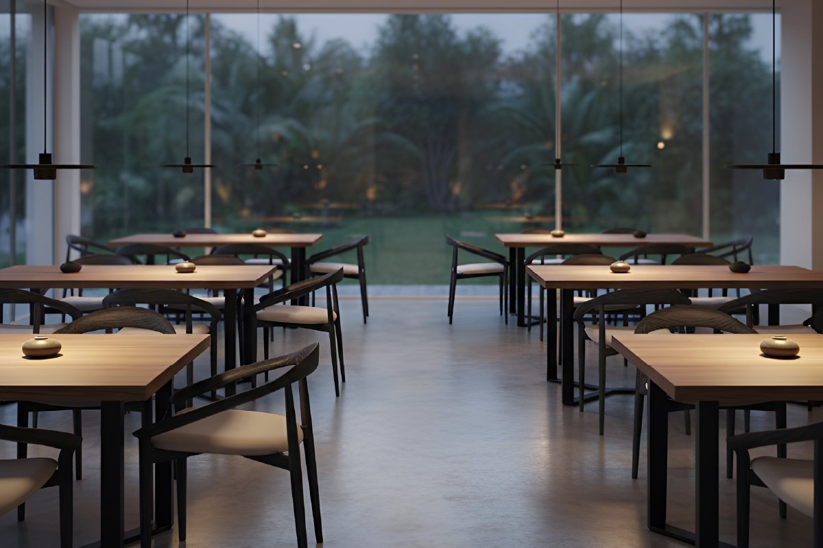 Interior of a high-end, minimalist restaurant furnished with custom teak wood furniture from a leading Indonesian furniture supplier. The space features square solid wood tables and matching dark-framed chairs with cream cushions, arranged symmetrically on a polished concrete floor. Large glass windows reveal a tranquil garden, enhancing the natural and sophisticated atmosphere sought by a premier hotel furniture supplier.