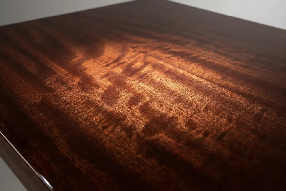 Close-up macro view of the deep, shimmering ribbon grain (chatoyancy) on mahogany Luxury Resort Furniture, demonstrating premium aesthetic quality.