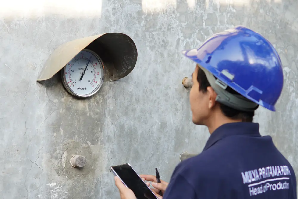 A furniture production manager inspecting a kiln drying facility, checking a large analog thermometer to monitor the temperature and reduce the moisture content of raw timber for manufacturing.