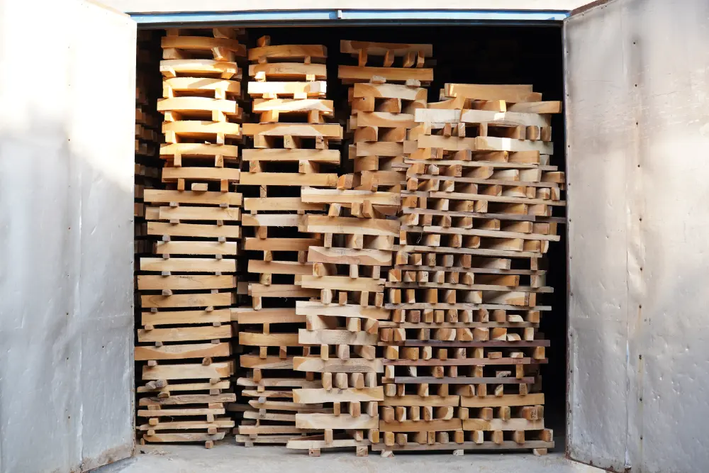 Stacks of rough-cut timber loaded into an industrial kiln dryer, arranged with spacers to allow airflow for even drying and uniform reduction of moisture content across the entire batch.