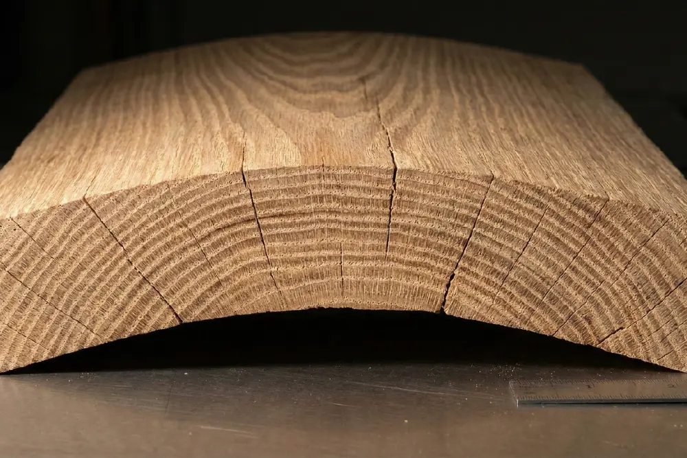Close-up end grain view of a thick oak board showing severe cupping and warping due to high wood movement risk and tangential shrinkage.