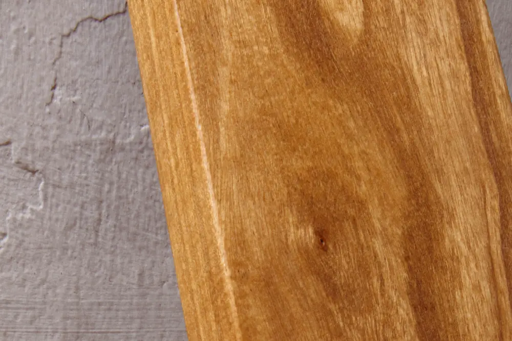 Close-up detail of a golden-brown teak wood plank showing natural grain patterns and texture, highlighting the premium material quality used in durable Indonesian outdoor furniture manufacturing.