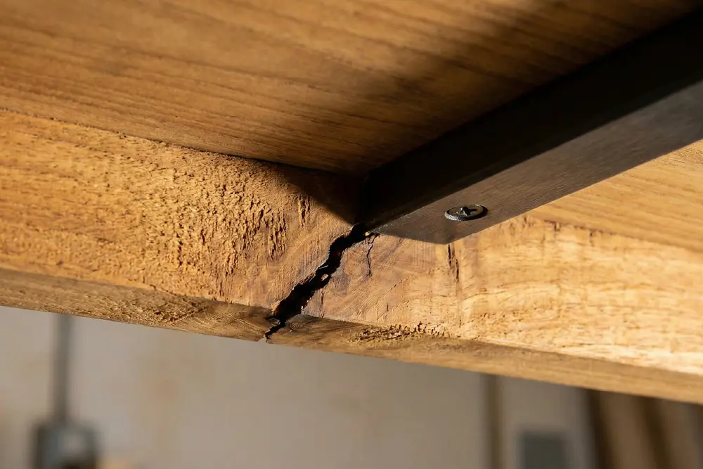 A close-up view of the underside of one of these Indonesian tables, showing a significant split and crack in the wood grain near a metal support beam.