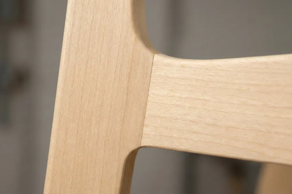 Macro close-up showing the precise joinery and smooth sanding of a blonde wood chair frame, proving the high-quality finish achieved when Indonesian furniture production is planned with realistic lead times to avoid defects.