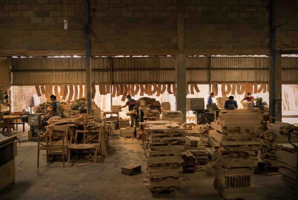 Wide view of a busy factory floor showing skilled craftsmen sanding and assembling wooden chair frames, highlighting the in-house production workflow used by Indonesian furniture manufacturers to maintain consistent export schedules.