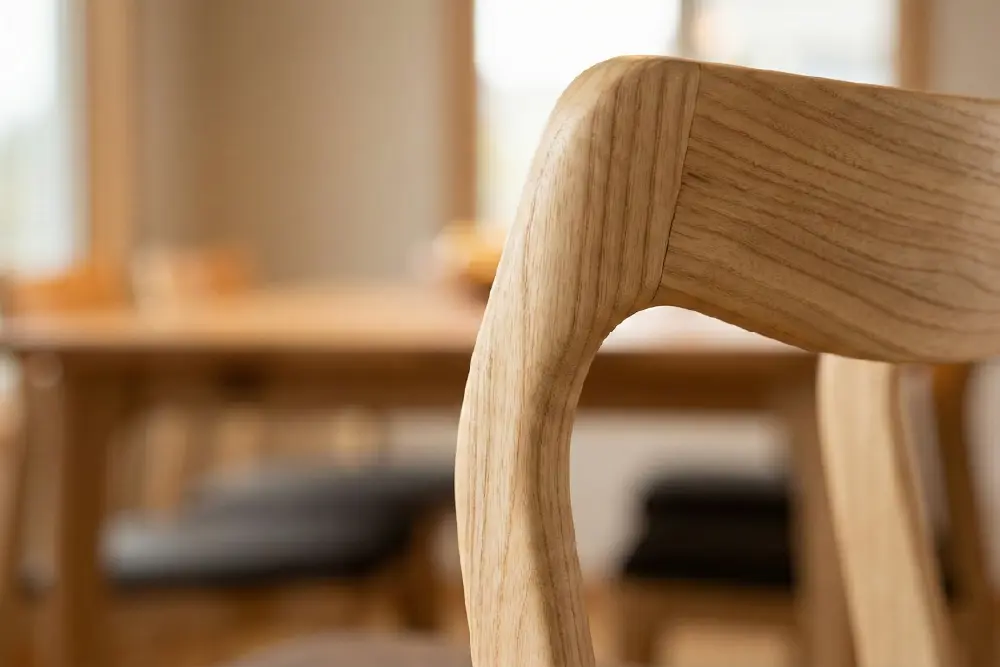 Detailed close-up of a dining chair's back leg joint, focusing on the smooth curve and precise joinery. The light-colored grain follows the chair's contours, emphasizing the high-quality craftsmanship of sungkai wood furniture.