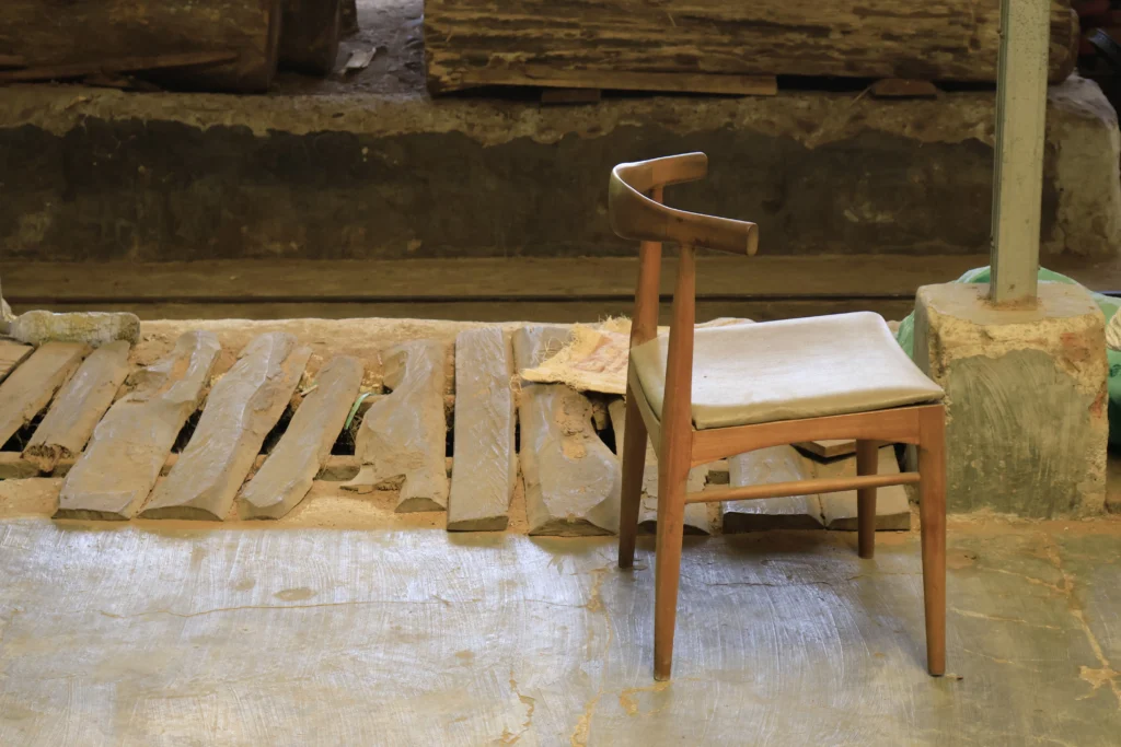 A solid wood chair frame sitting in an Indonesian timber workshop, illustrating the robust foundation of durable furniture for retailer costs savings through long-lasting raw materials.