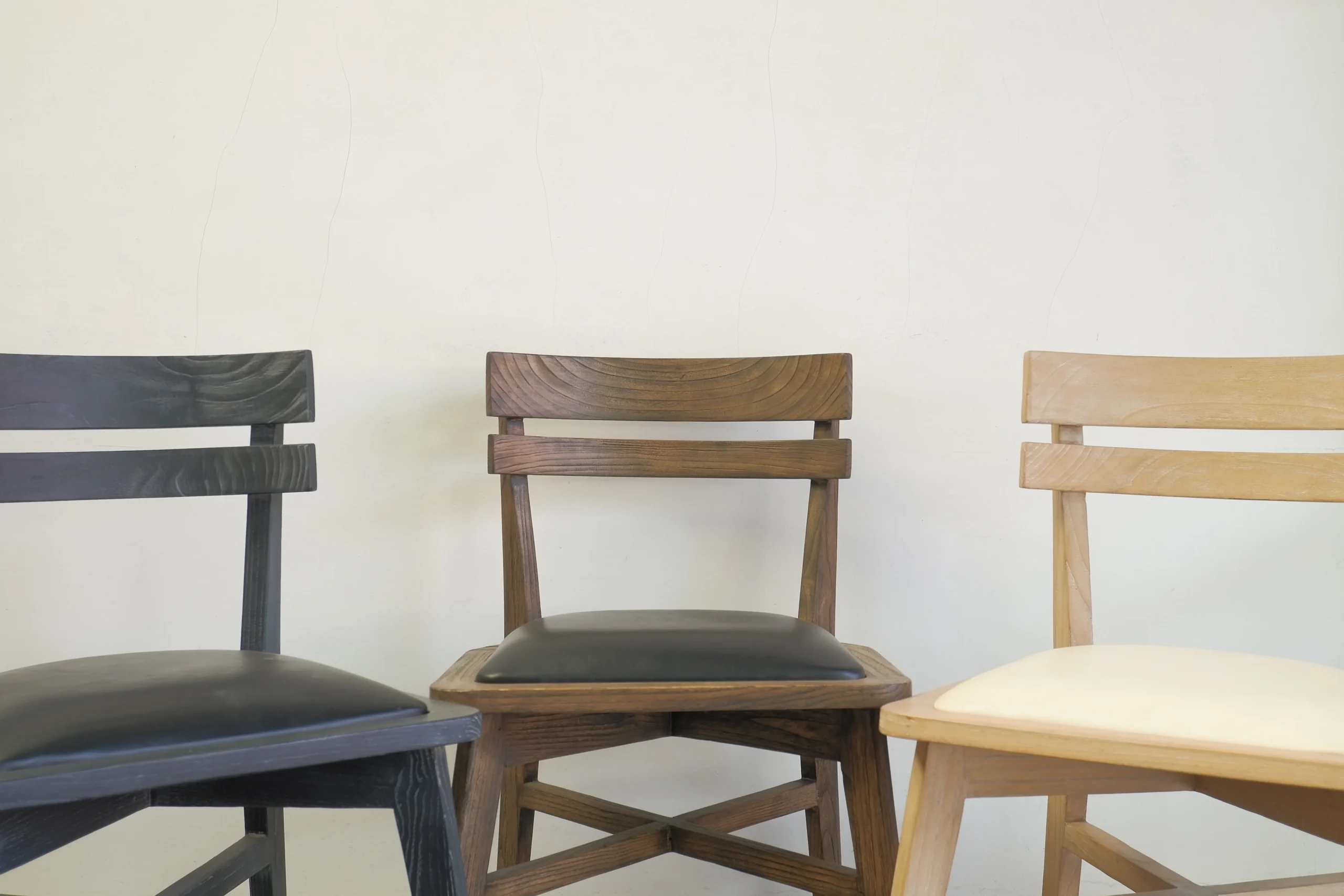 Three high-quality solid wood dining chairs with different finishes displayed together, exemplifying how investing in durable furniture for retailer costs leads to long-term savings and consistent showroom aesthetics.