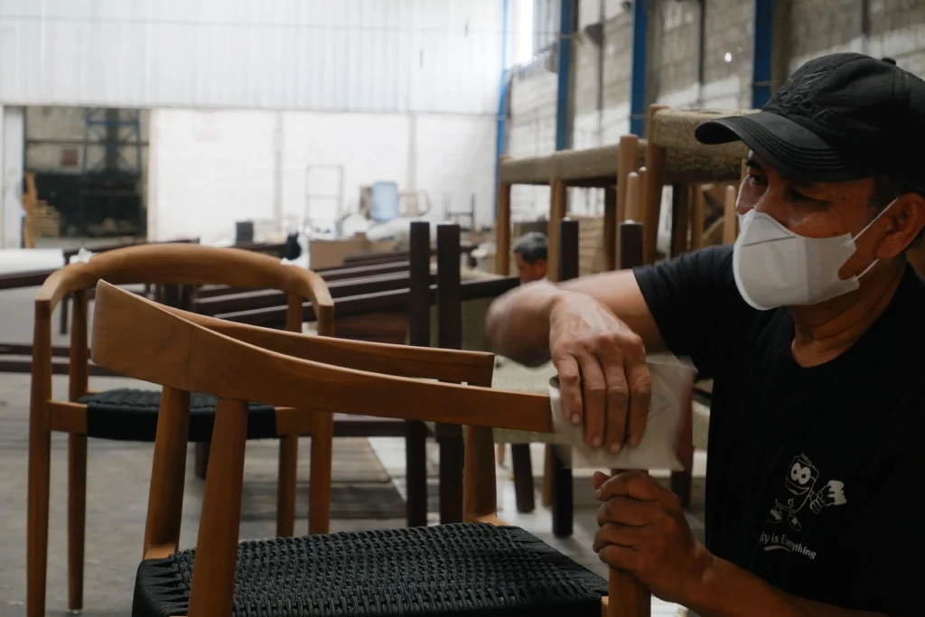 An Indonesian craftsman hand sanding a wooden chair during the production phase that impacts lead times for managing furniture inventory