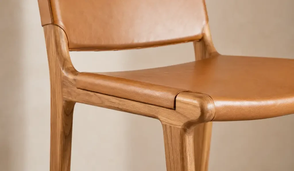 Close-up of light Sungkai wood grain paired with cognac leather on a counter stool