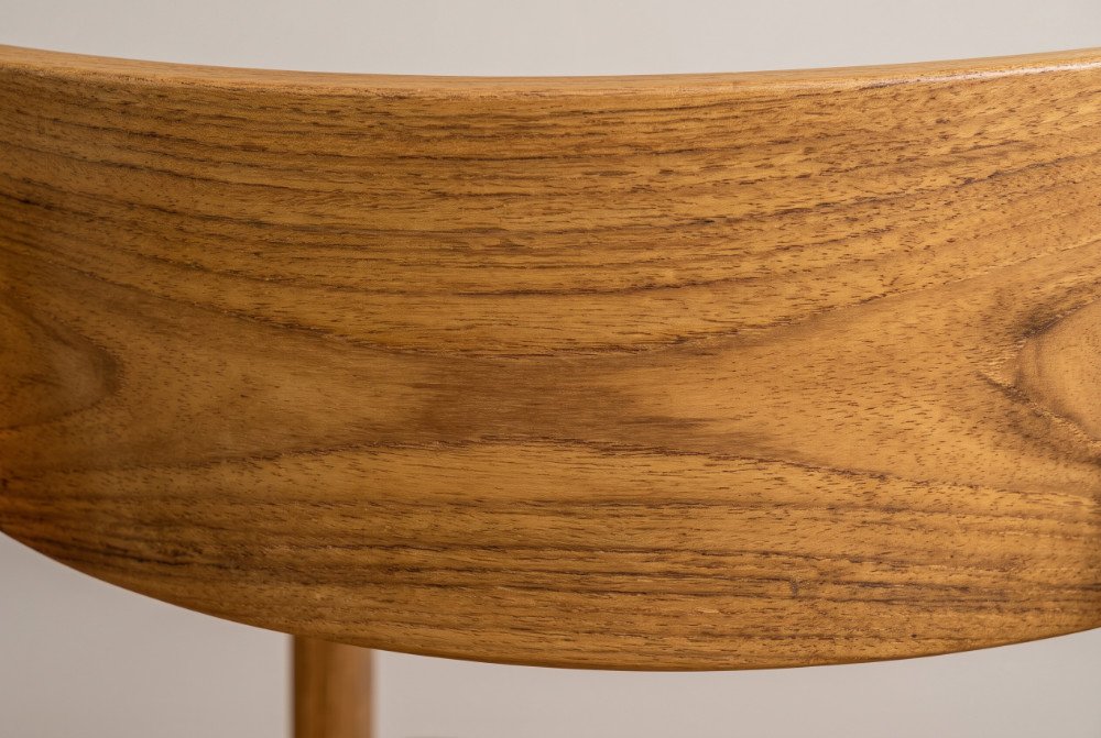 A close-up photo of the rich, natural, golden-brown heartwood grain texture on the backrest of a teak dining chair.