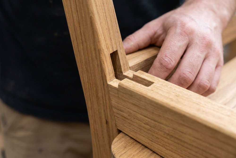 A detailed macro shot of a precise mortise-and-tenon joint at the base of a teak dining chair leg, showcasing its structural strength.